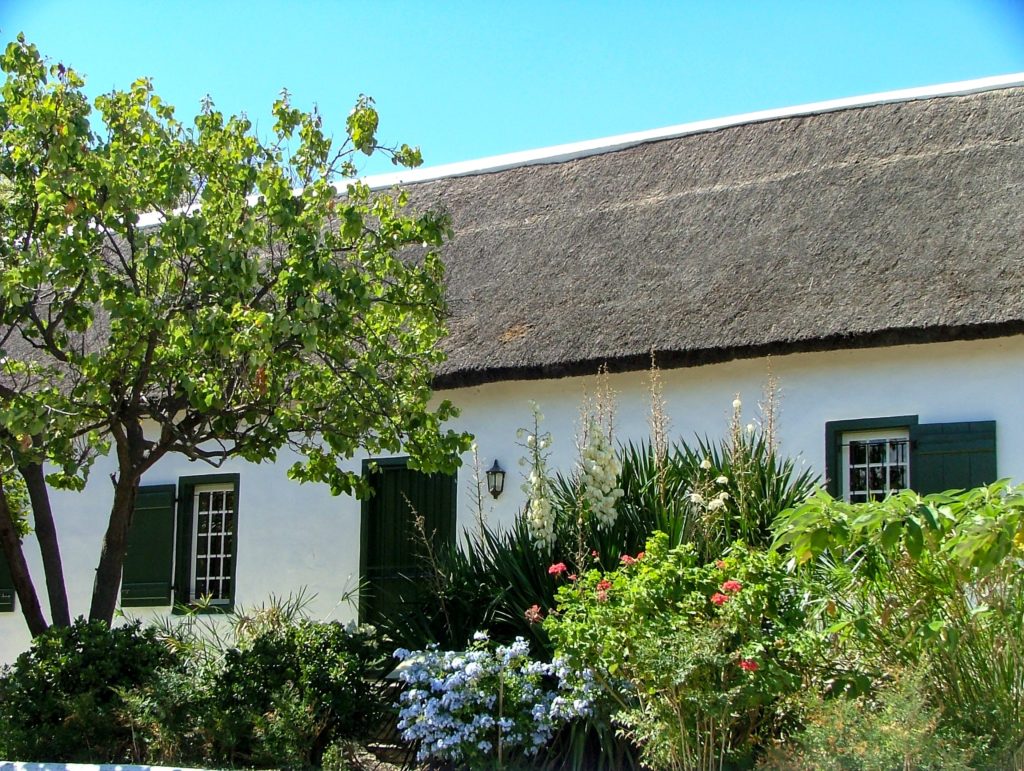 Photo of a thatched cottage with trees and flowers outside