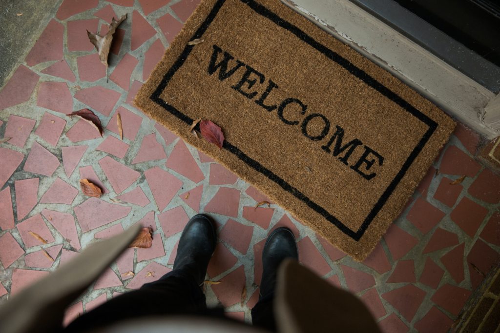 Photo of a doormat saying "Welcome" with a person's boots visible next to it