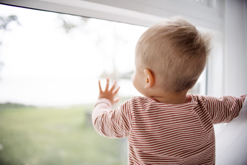 Photo of little boy standing with his hand pressed against a glass door