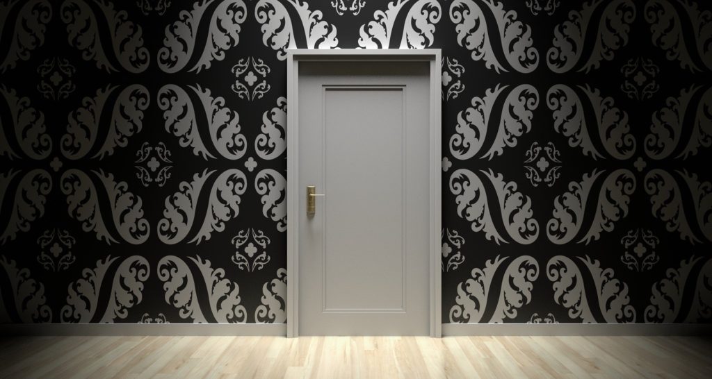 Photograph of a closed white door on a wall with black and white patterned wallpaper