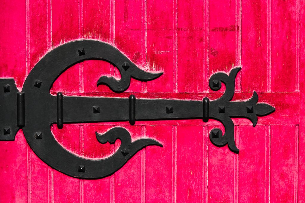 Photograph of red door with black decorative metal hinge