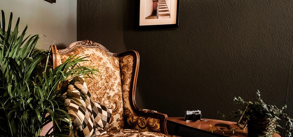 a high backed tradtional arm chair against a painted wall with photo frames. A victorian-inspired living area.